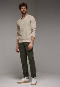 Béžový pletený svetr s límečkem, doplněný olivově zelenými zúženými kalhotami a bílými teniskami. Texturovaná látka, ležérní design.