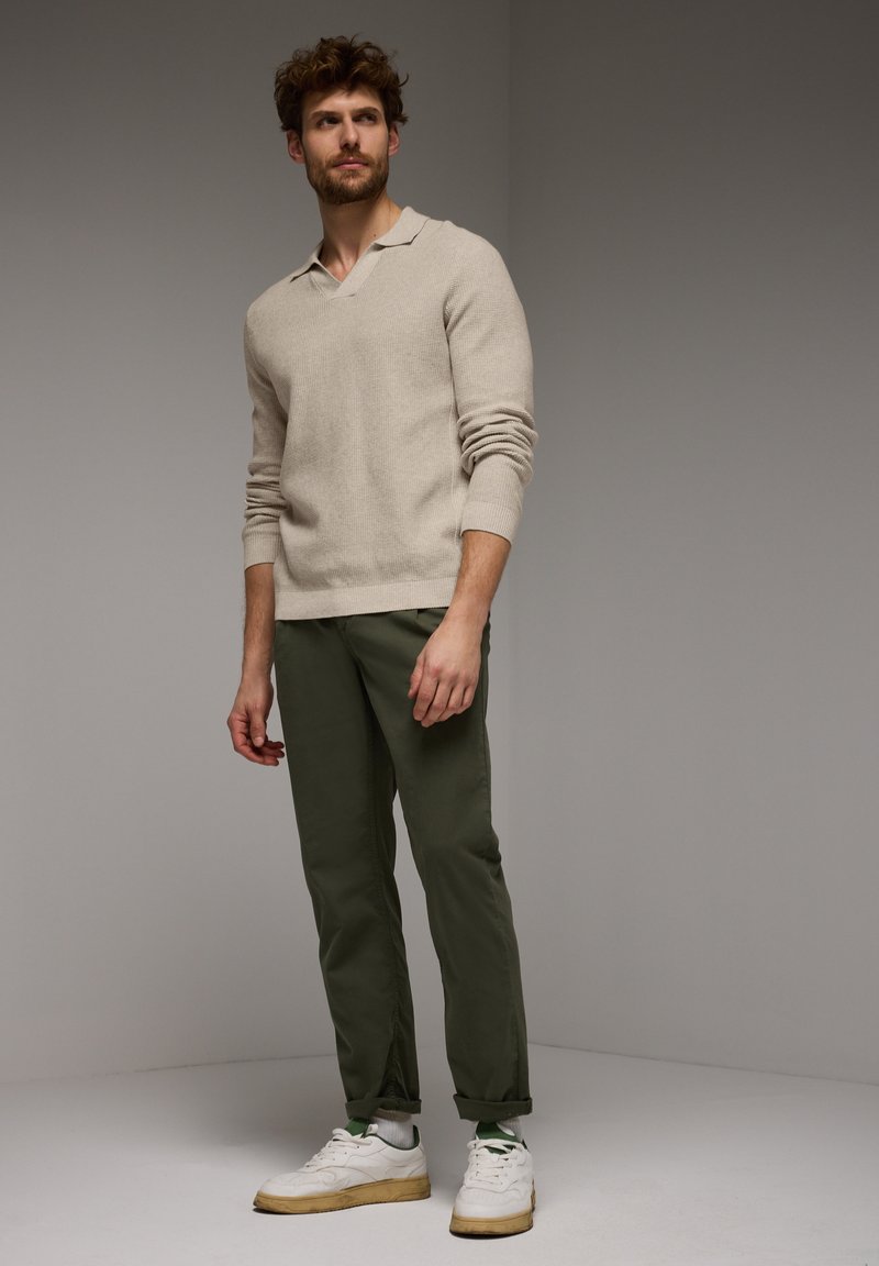 Béžový pletený svetr s límečkem, doplněný olivově zelenými zúženými kalhotami a bílými teniskami. Texturovaná látka, ležérní design.