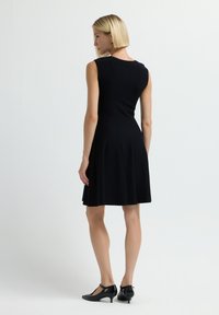 Vestito nero senza maniche con gonna a ruota, realizzato in tessuto morbido. Presenta cuciture verticali e una trama sottile. Abbinato a tacchi neri.