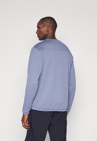 Μπλε μακρυμάνικη μπλούζα με υφή, διαθέτει στρογγυλή λαιμόκοψη και ραφές στην πλάτη. Το ύφασμα φαίνεται ελαφρύ και αναπνεύσιμο.