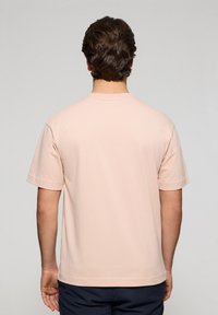 Camiseta de algodón color rosa claro con mangas cortas y escote redondo, con una textura suave y un diseño sencillo. Se muestra la vista trasera.