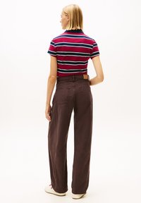 Camiseta polo a rayas en rojo, azul marino y blanco, combinada con pantalones marrones sueltos. Cuenta con mangas cortas y una etiqueta de cuero en la cinturilla.