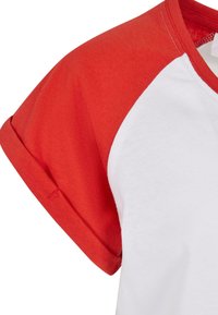 Hvit t-skjorte med korte, røde raglanermer. Stoffet ser mykt ut med synlige sømmer langs kragen og ermene.