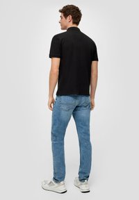 Czarna koszulka polo z krótkim rękawem, w zestawieniu z jasnoniebieskimi dżinsami i białymi trampkami. Polo ma klasyczny design i minimalne detale.