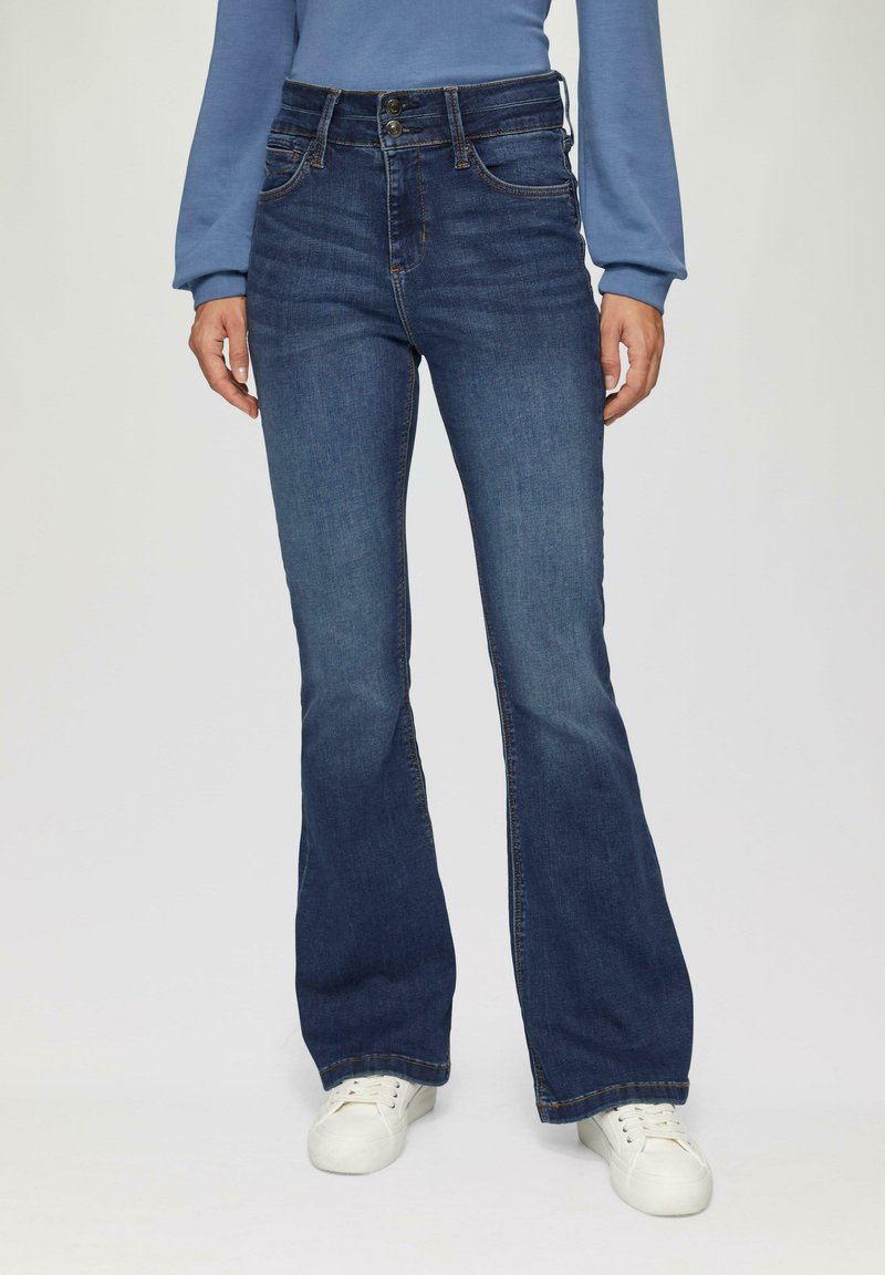 Blauwe flared jeans van denim met een hoge taille, voorzien van een dubbele knoopsluiting en voorkruiden, gecombineerd met witte sneakers.