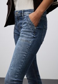 Jeans ajustados de mezclilla azul con un ligero desvanecimiento, que presentan bolsillos frontales, herrajes plateados y una tela texturizada.