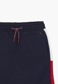 Pantaloncini in pile blu navy con vita a coulisse. Presentano strisce laterali bianche e rosse. Tessuto morbido e vita elasticizzata per il massimo comfort.