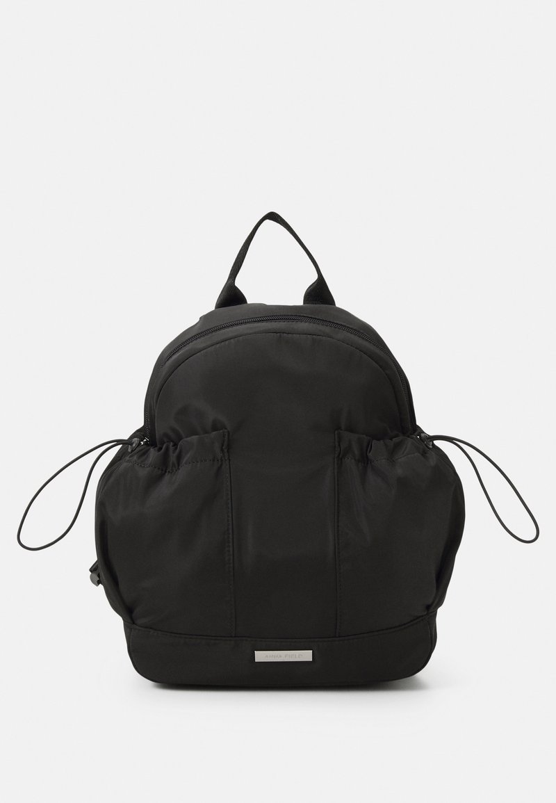 Mochila de nylon negra con forma redondeada, cierre de cremallera, dos bolsillos laterales elásticos y un asa en la parte superior. Diseño minimalista con sutiles acentos de hardware.