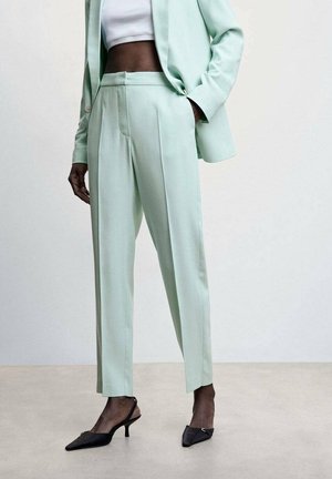 Mujer con pantalones verdes claros a medida y blazer a juego, top corto blanco y tacones slingback negros con punta afilada.