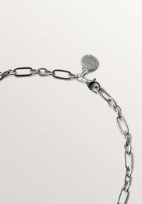 Pulsera de cadena de plata con eslabones ovalados alargados, un cierre de langosta y una etiqueta circular, todo con un acabado pulido.