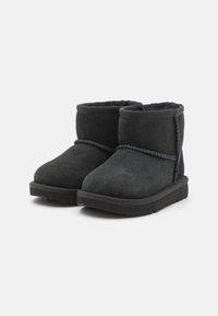 Bottines en daim noir avec une doublure intérieure douce, une semelle extérieure texturée et des coutures décoratives autour de la cheville. Forme classique de bottines.