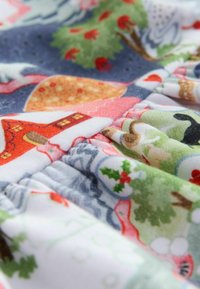 Buntes Baumwollgewebe mit festlichem Muster aus Häusern, Bäumen und Tieren in Rot-, Grün- und Blautönen. Weiche, strukturierte Oberfläche.