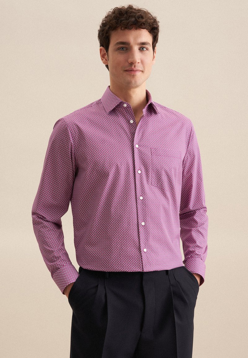 Camicia a maniche lunghe di un rosa scuro con un motivo geometrico bianco, chiusura con bottoni sul davanti, colletto aperto e una tasca sul petto. Tessuto in cotone.