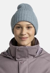 Light blue knitted beanie with a ribbed texture and a tapered top, paired with a purple collared jacket featuring snap buttons.
