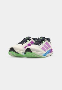 Scarpe sportive con una tomaia in rete bianca, accenti viola, suole verdi e blu, con lacci neri e dettagli di branding.