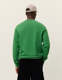 Žalia sportinė palaidinė su apvaliu kaklu ir gipiūriniais rankogaliais, derinama su juodais velveto kelnėmis ir smėlio spalvos juostine kepure.