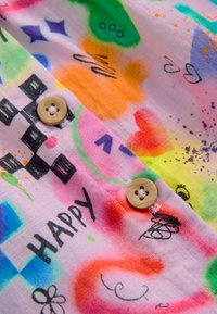 Tessuto colorato con motivi astratti, caratterizzato da tonalità di arancione, verde, rosa e blu. Due bottoni di legno con quattro fori sul colletto.