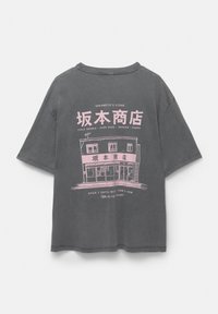 Šedé oversized tričko s růžovou grafikou obchodu, která obsahuje text s popisem produktů a otevíracích hodin. Krátké rukávy.