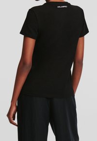 Černé bavlněné tričko s kulatým výstřihem a krátkými rukávy, se skromnou značka na zadní straně výstřihu. Hladká textura, standardní střih.
