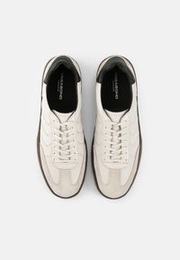 Hvite lær- og semsket skinn sneakers med svarte hæl-detaljer, rund tå og snøring. Har teksturerte paneler og logo på sålen.