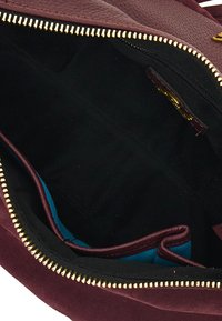 Interno di una borsa in pelle borgogna con zip dorata, foderato in tessuto nero e una sezione di accentuazione blu su un lato. Dettagli di design minimalisti.