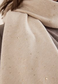 Écharpe beige en tricot doux, ornée de petits accents métalliques dispersés pour ajouter de la texture et un intérêt visuel.