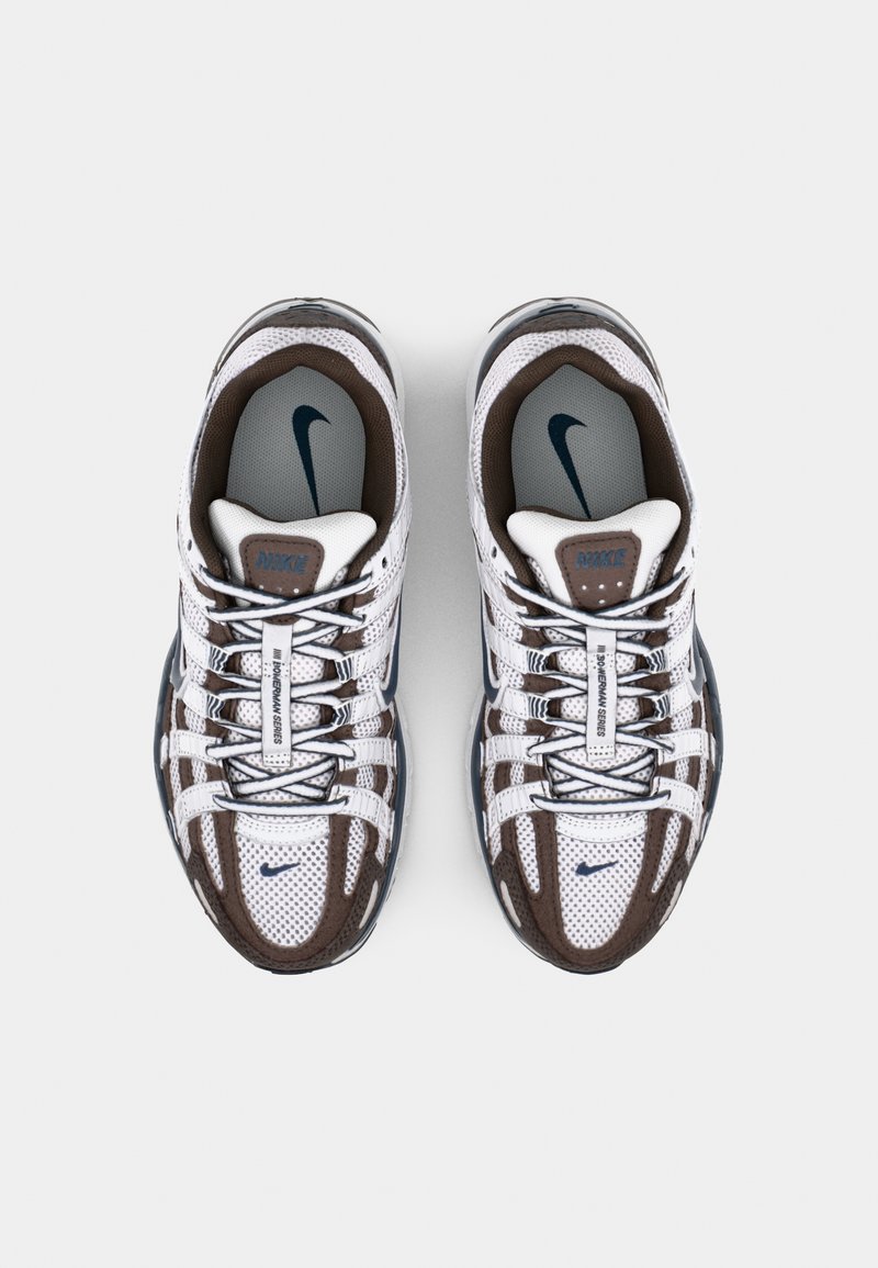 Nike sneakers met een witte mesh bovenkant, bruine accenten, blauwe details en een opvallend vetersysteem. Heeft een gevoerde kraag en logo.