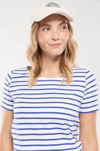 Pasiasta koszula z krótkim rękawem w białym i niebieskim kolorze, w połączeniu z kremową czapką z granatowym logo. Gładki materiał, luźny krój.