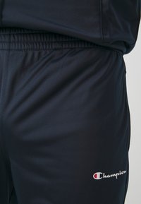 Pantaloni sportivi navy con vita regolabile tramite cordino e dettaglio del logo in bianco. Tessuto liscio e leggero con una leggera brillantezza.