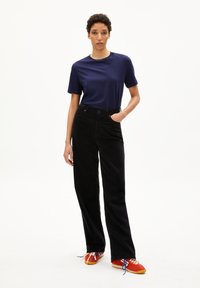 Marineblaues Kurzarm-T-Shirt, hoch taillierte schwarze Cordhosen und rote Sneakers mit blauen und weißen Schnürsenkeln. Glattes Material, lässige Passform.