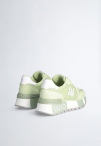 Sneakers verde chiaro realizzati in materiali mesh e suede, con tallone e logo bianchi, suola chunky con accenti a bande verdi e bianche.