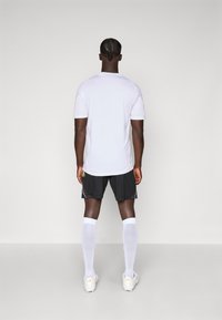 Hvit atletisk T-skjorte, svarte shorts med rosa detaljer, hvite knelange sokker og hvite fotballsko. Designet er funksjonelt for sport.