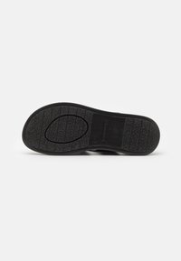 Suola nera di scarpa con gomma testurizzata per la presa. Presenta scanalature e un design ovale, contrassegnato da dettagli del logo per trazione e durata.