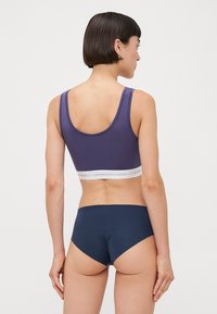 Lila, zökkenőmentes bralette széles vállpántokkal és fehér márkázott pánttal; párosítva tengerészkék, magas derekú bugyival, sima textúrával.