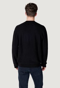Maglione nero con motivo testurizzato, collo a giro, polsini e orlo a coste, abbinato a jeans blu scuro. Vista posteriore che mostra la sua vestibilità rilassata.