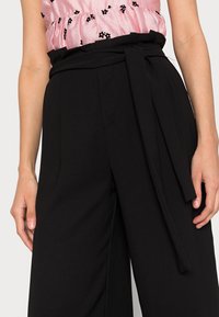 Pantalon noir taille haute à jambes larges, doté d'une ceinture assortie à la taille et d'une finition en tissu lisse.