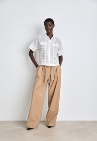 White button-up shirt with lace pattern, paired with beige high-waisted trousers, creating a relaxed, tailored silhouette and sharp black heels.
