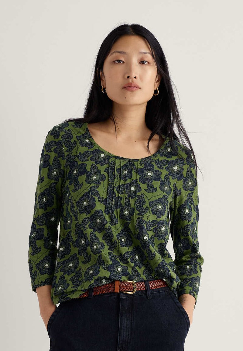 Roheline lillemustriga pluus, millel on kolmveerandvarrukad, kaelusel volditud laskmed ja tume sinine lillemuster valgete aksentidega.