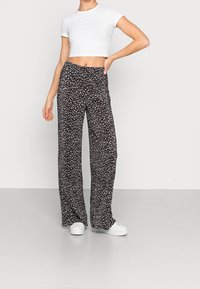 Pantalon large à imprimé floral noir en tissu respirant, accompagné d'un t-shirt court blanc et de baskets blanches.