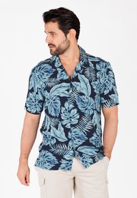 Korte mouwen shirt gemaakt van lichtgewicht stof, met een marineblauwe achtergrond en grote, lichtblauwe tropische bladerenpatronen.