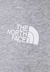 Logo blanc "The North Face" imprimé sur un tissu tricoté gris, montrant le nom de la marque et un graphisme demi-dôme.