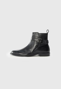 Botas de cuero negro hasta el tobillo con puntera redondeada, detalle de hebilla lateral y una pestaña en el talón. Suela plana con un acabado sutilmente brillante.