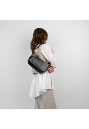 Borsa a spalla nera in pelle effetto coccodrillo con dettagli dorati, caratterizzata da una texture morbida e una forma strutturata, indossata su un outfit leggero a strati.
