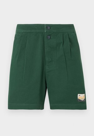 Sötétzöld, pliszírozott rövidnadrág két első gombbal és egy kis téglalap alakú folttal a bal lábán, a szegély közelében.