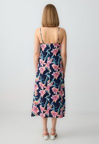 Marineblaues Midikleid mit pinkem Blumenmuster, dünnen Schulterträgern und geradem Saum; getragen mit weißen Blockabsatzsandalen.
