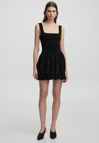 Robe noire avec un décolleté carré, un corsage ajusté et une jupe volumineuse à volants. Le matériau semble lisse, avec une texture légèrement brillante.