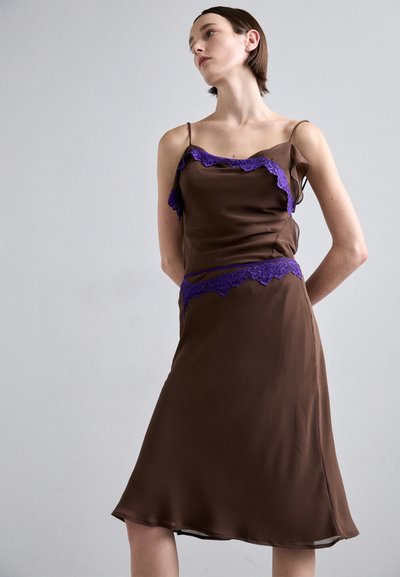 Abito in satin marrone con dettagli in pizzo viola lungo il scollo e la vita, caratterizzato da spalline sottili e una silhouette A-line fluida.