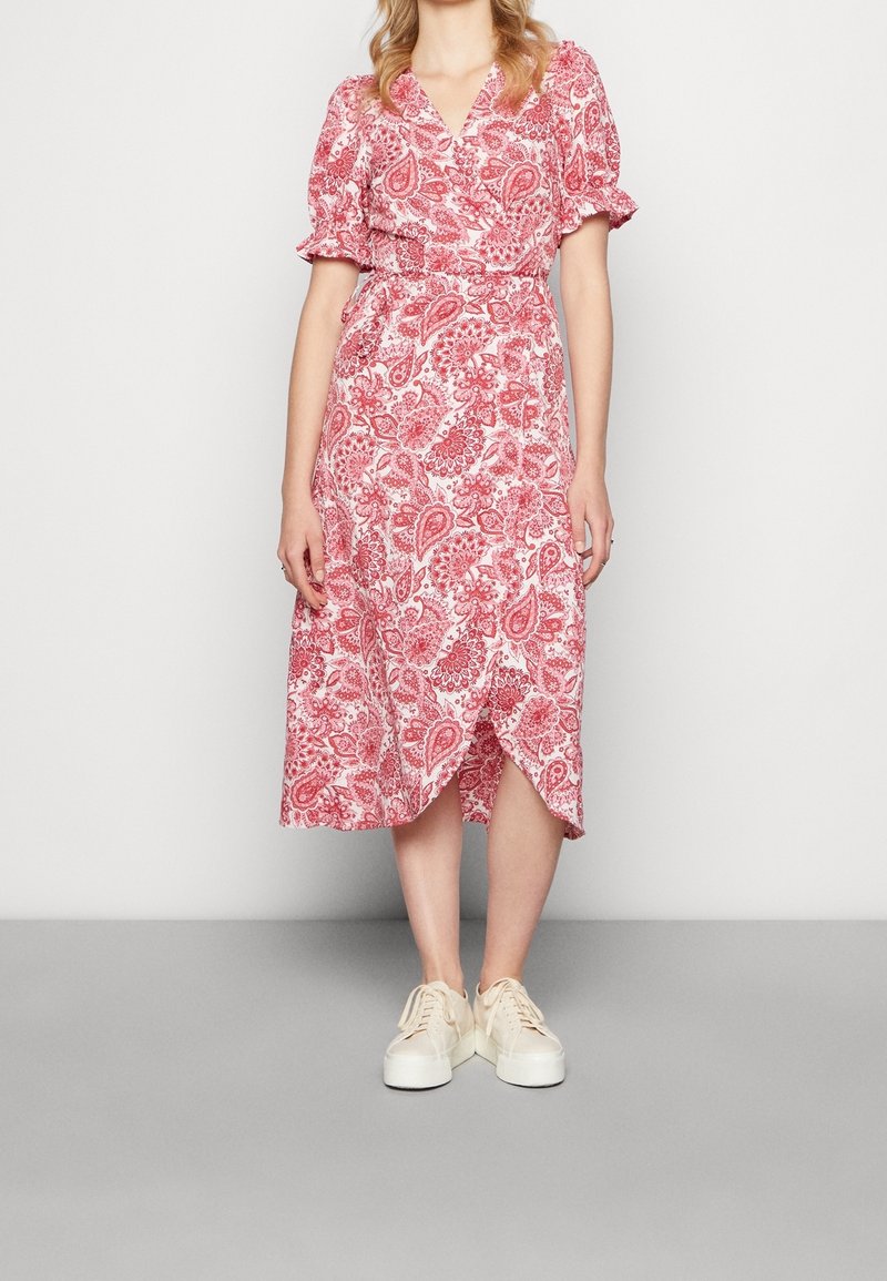 Robe midi rouge à motif cachemire avec manches courtes bouffantes, un décolleté en V profond et un design portefeuille, associée à des baskets blanches.