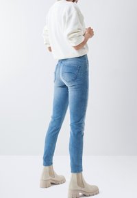 Vaqueros ajustados de color azul claro con un corte clásico, que presentan dos bolsillos traseros y detalles de costura. Combinados con un suéter de punto en color crema y botines beige.