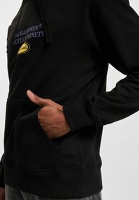Felpa nera con finitura testurizzata, dotata di una tasca frontale e un logo ricamato in viola e giallo sul petto.
